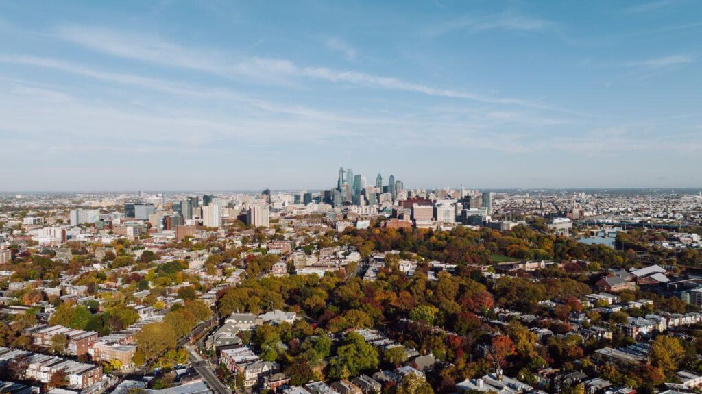 Aerial view of the Philadelphia skyline rising above tree-lined neighborhoods in fall colors, the starting point for a long American road trip
